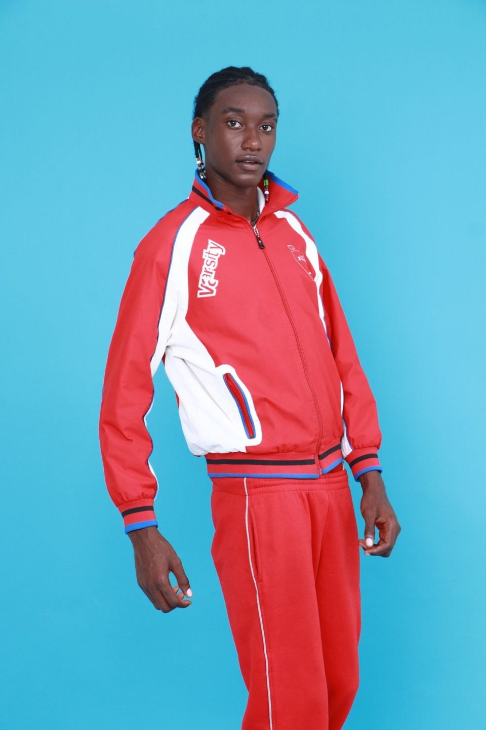 A young man in a red and white retro tracksuit against a blue background